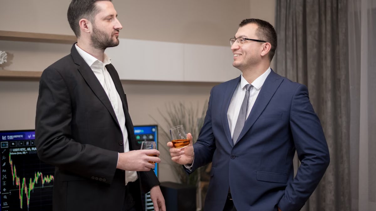Two business professionals socializing indoors, wearing formal attire, engaging in a friendly conversation.